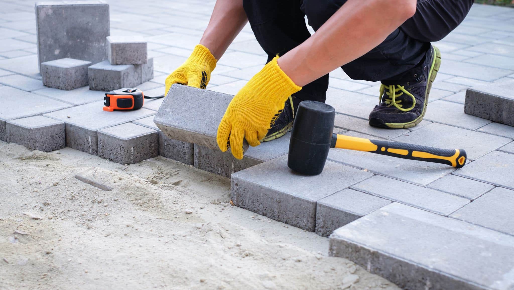Pflasterarbeiten mit Betonsteinen und Gummihammer auf Gehweg im Außenbereich