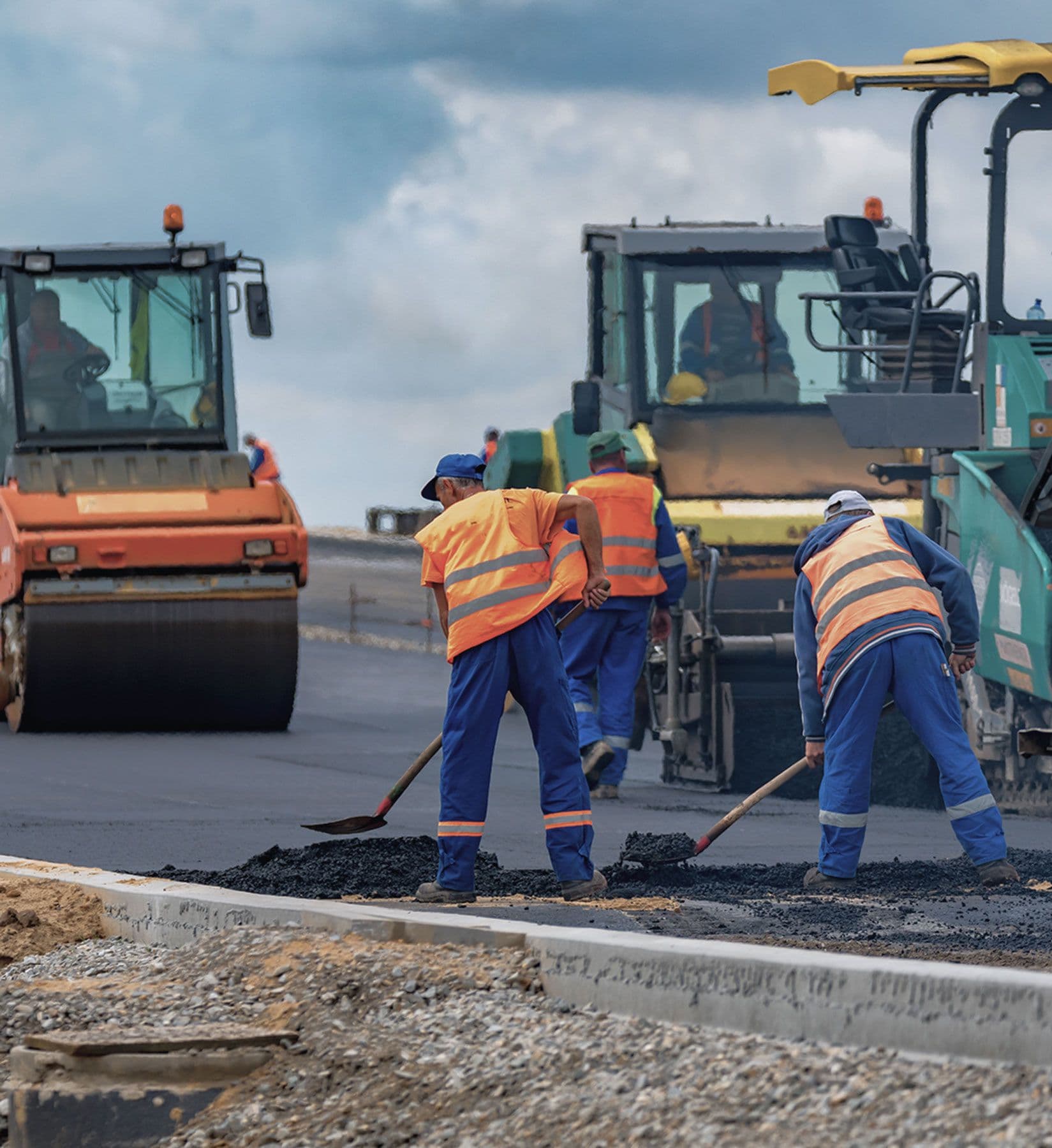 Bauarbeiter verteilen frischen Asphalt bei Straßenbauarbeiten mit Walzen im Hintergrund