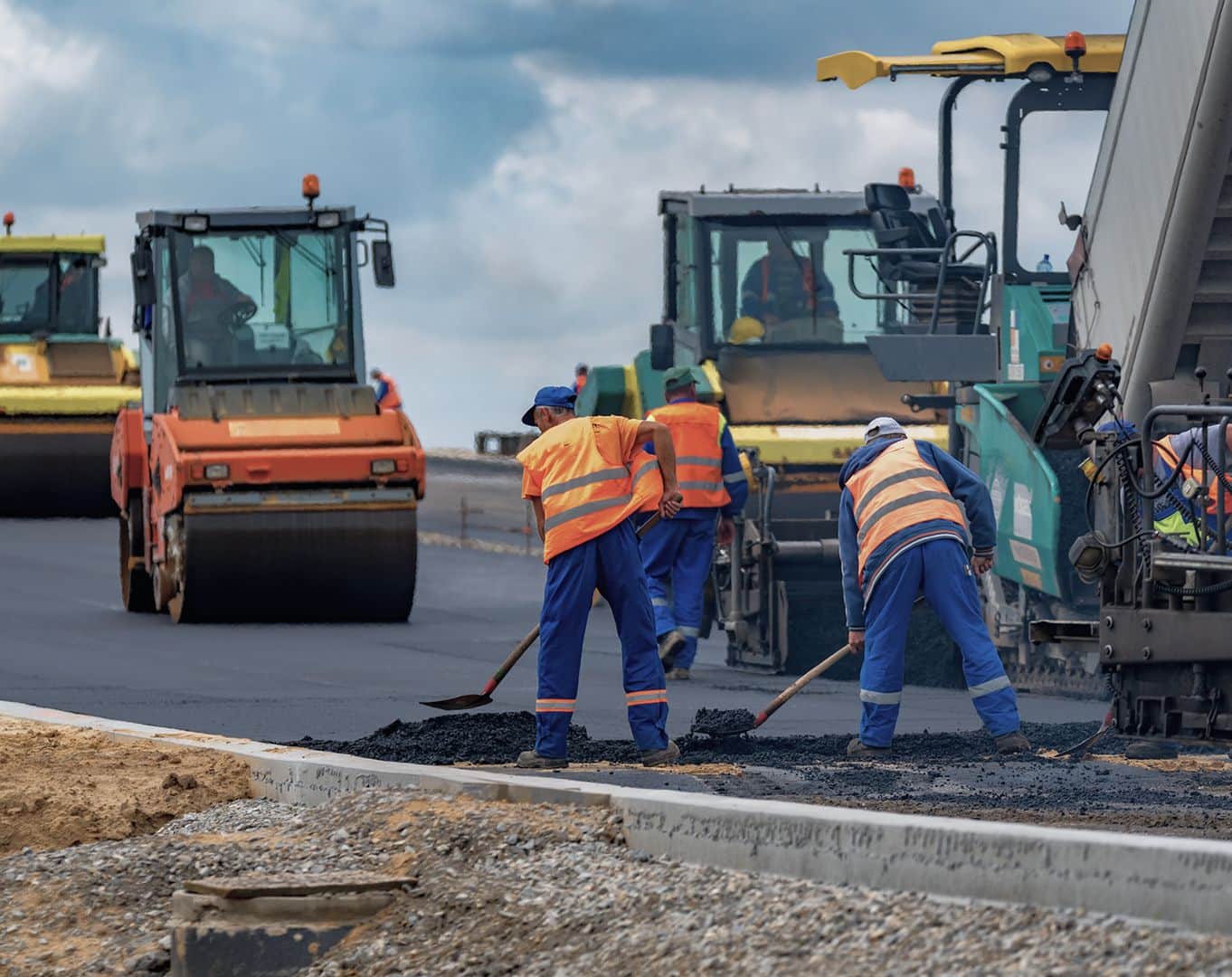 Arbeiter asphaltieren eine Straße mit großen Baumaschinen unter wolkenlosem Himmel