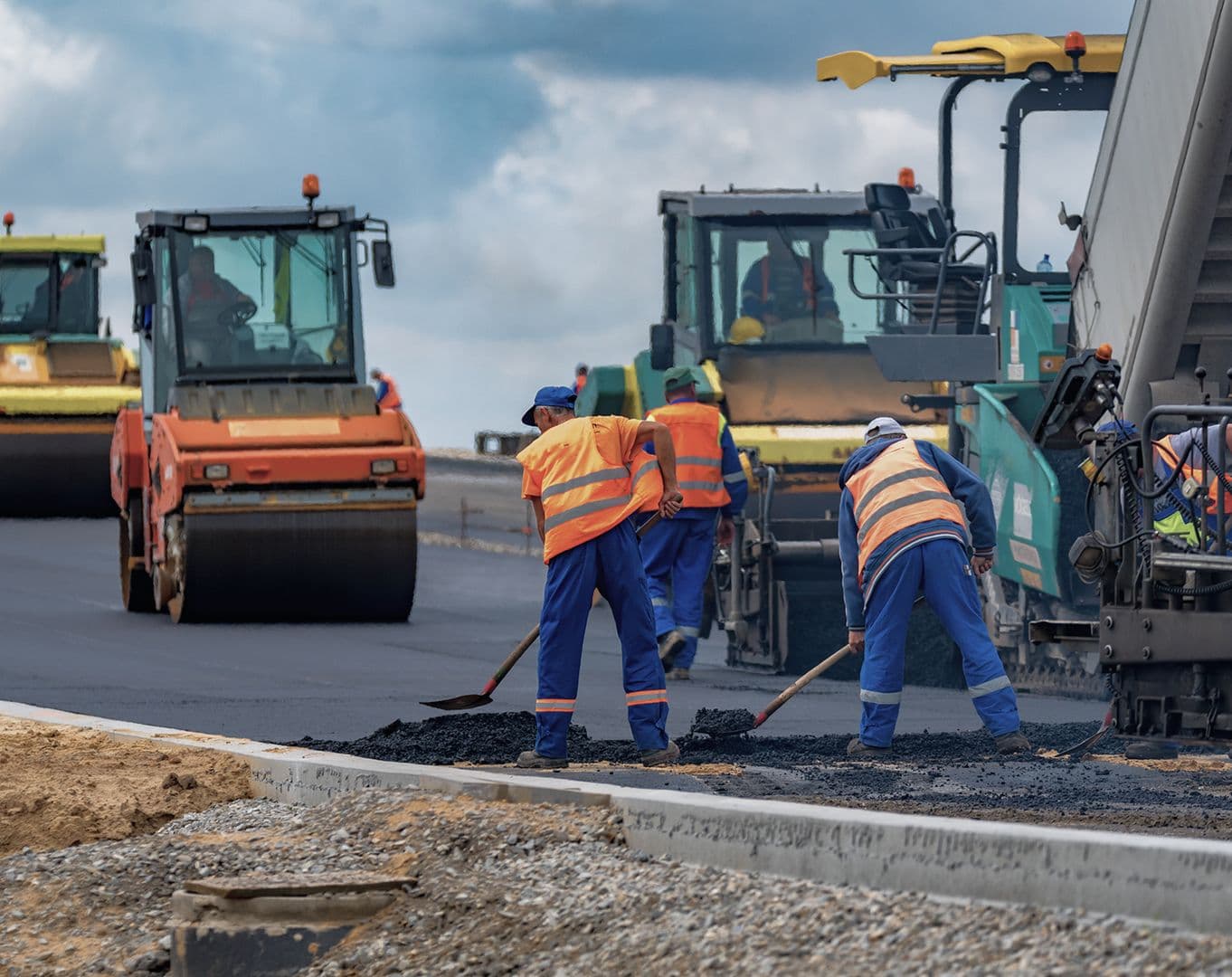 Arbeiter asphaltieren eine Straße mit großen Baumaschinen unter wolkenlosem Himmel